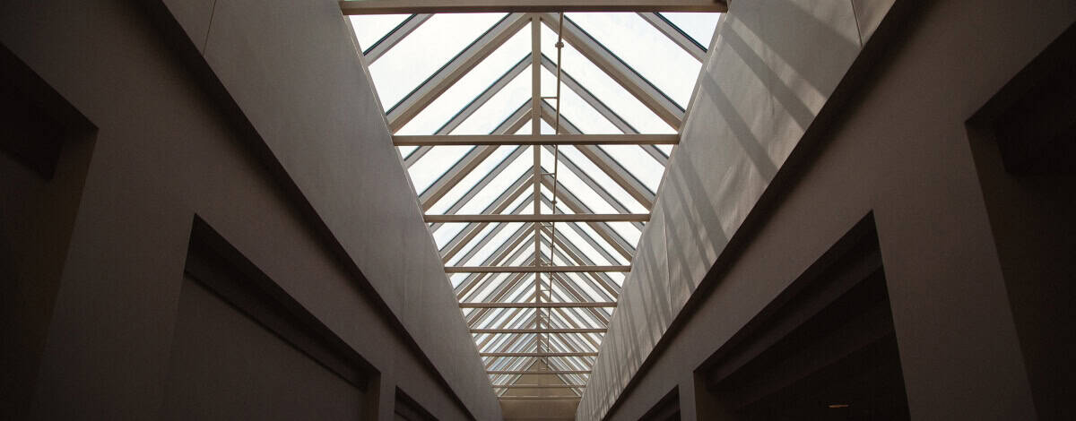 Angled view of a corridor with a glass-paneled, triangular skylight roof, allowing natural light to illuminate the space below.